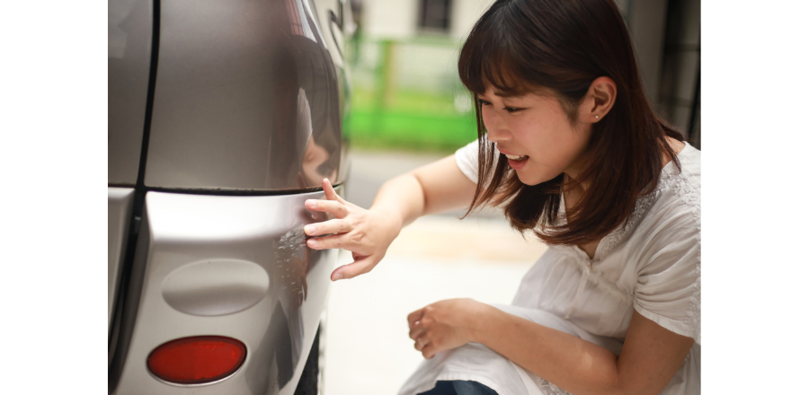 車のバンパーについた小さなキズを、女性が指で確認している様子